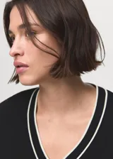 Jersey de punto fino color negro con cuello de pico y ribetes en contraste blanco en el cuello y puños. Diseño recto y manga larga.