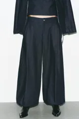 Pantalón bombacho de denim azul oscuro, tiro medio, con bolsillos laterales ocultos y de parche en la espalda. Presenta pinzas en la parte delantera y bajo abullonado con elástico.