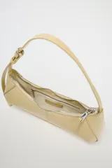 Bolso de hombro color crema, con forma alargada y asa ajustable con hebilla. Tiene pespuntes en el cuerpo, bolsillo interior con cremallera y cierre principal con cremallera y tirador.