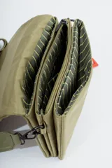 Bandolera color verde oliva con correa de tela ajustable con el nombre de la marca estampado. Incluye un dije colgante con forma de corazón.