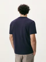 Camiseta blanca de algodón con cuello redondo y mangas cortas. Estampa rectangular con borde negro que contiene la frase "NATURAL ATMOSPHERE" en letras mayúsculas y una imagen de montañas y mar.