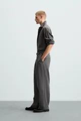 Pantalón negro de corte amplio con cinturón de tela con hebilla metálica. Presenta pliegues frontales, bolsillos laterales y traseros. Cierre frontal con cremallera y botón.