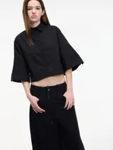 Camisa cropped negra con botones en la parte delantera y mangas 3/4 acampanadas con botones. Presenta pinzas en la espalda.