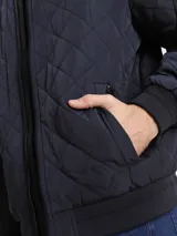 Campera bomber azul marino con diseño acolchado en forma de rombos, cierre frontal con cremallera, cuello, puños y dobladillo acanalados, bolsillos laterales y bolsillo en la manga con cremallera. Logotipo de Calvin Klein en la manga.
