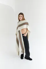 Ruana artesanal color beige con rayas horizontales rojas y amarillas, y flecos en el borde inferior.