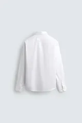 Camisa blanca de corte regular fit, con cuello italiano, manga larga con puños abotonados y cierre frontal con botones.
