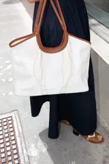 Bolso tipo tote de tela color crudo con detalles de cuero marrón en las asas y la base.