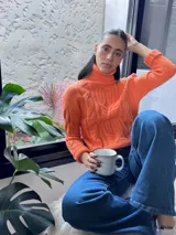Polera elastizada color naranja con cuello alto y diseño trenzado.