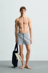 Bañador de hombre confeccionado en tejido técnico con textura. Diseño a rayas verticales en tonos azul y blanco. Cintura elástica ajustable con cordón. Bolsillos laterales y detalle de bolsillo trasero de solapa. Bajo con aberturas laterales. Forro interior.