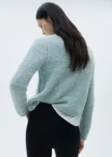Chaqueta color celeste de tejido bouclé con cuello redondo, cierre frontal con botones efecto joya, dos bolsillos de parche frontales y mangas largas.