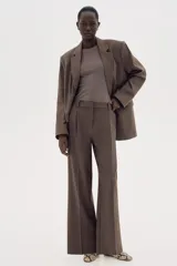 Pantalón sastrero marrón de corte holgado con tiro alto y cierre con corchete y botón ocultos. Piernas amplias con pinzas, pliegues adelante y atrás, bolsillos al bies y bolsillos decorativos atrás.