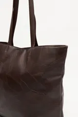 Cartera tipo tote color marrón oscuro, con diseño de parches de cuero texturizado y asas largas.