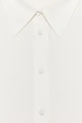 Camisa marrón de corte holgado, con cuello de solapa, manga larga con pliegues y bajo asimétrico. Cierre frontal con botones.