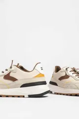 Zapatillas deportivas color beige con detalles en marrón y amarillo.