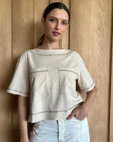 Remera color crema con cuello redondo y mangas cortas, con dos bolsillos cuadrados en el frente y costuras a contratono.