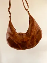Cartera bandolera tipo hobo de cuero color marrón chocolate, con correa ajustable y cierre superior con cremallera.