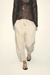 Pantalón color beige de tiro medio con cintura elástica ajustable con cordones, bolsillos delanteros y falsos bolsillos de vivo en la espalda. El bajo es ajustable con botón a presión.