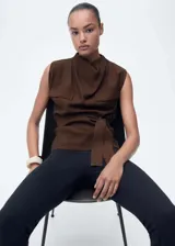 Blusa marrón sin mangas con cuello drapeado, trabillas, dos bolsillos de solapa en el pecho, cinturón desmontable y cierre de botón en la parte posterior.