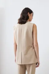 Chaleco largo color beige con solapas, sin mangas y con un botón metálico.