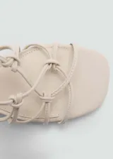 Sandalias color beige con tacón bloque y tiras finas que se atan alrededor del tobillo.