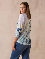 Buzo blanco estampado con flores azules y detalles en verde y amarillo, de la marca Milano. Tiene cuello redondo y mangas 3/4 con apliques de brillos en el frente.