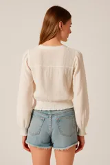 Blusa color blanco con cuello redondo, mangas largas con puños elásticos y cierre frontal con botones.