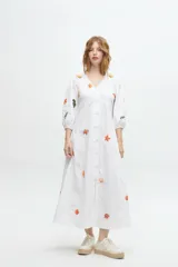 Vestido midi color arena con escote en V, mangas 3/4 abullonadas y cierre frontal con botones. Presenta bordados de motivos marinos.