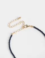 Collar corto de mostacillas azul marino con dije de corazón blanco y detalles dorados.
