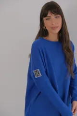 Buzo azul de viscosa con cuello redondo y manga larga. Presenta un aplique con diseño geométrico en el brazo izquierdo.