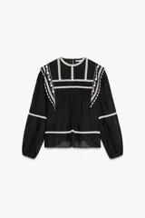 Blusa negra de algodón con cuello redondo y manga larga abullonada. Presenta bordados blancos a contraste en el cuello, hombros y mangas. Cierre en la espalda con abertura y botón.