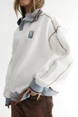Buzo celeste con cuello polo y puños en rib color verde lima. Tiene un parche con el logo de la marca en el pecho y rayas horizontales en el ruedo.