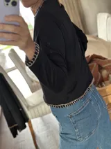 Remera negra de algodón con cuello redondo y bordados blancos en cuello, puños y ruedo. Corte recto.