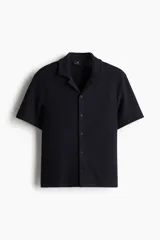 Camisa azul marino de manga corta en tejido de punto con textura. Tiene cuello resort, tapeta con botones y corte recto.