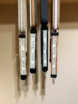 Correa de tela beige con rayas blancas y negras, con mosquetones metálicos plateados y apliques de cuero sintético negro.