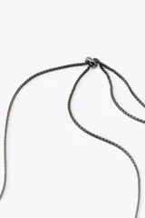 Collar tipo babero con flecos de piezas metálicas doradas y cadena de eslabones negros.
