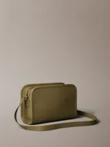 Cartera cruzada de piel sintética color verde oliva, con silueta rectangular y bordes pespunteados. Presenta un monograma tonal de Calvin Klein grabado en relieve en la parte delantera. Incluye correa ajustable para llevar al hombro o cruzada y cierre de cremallera superior.