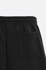Bermuda negra relaxed fit confeccionada en tejido interlock de algodón con elasticidad. Cintura elástica ajustable con cordón. Bolsillos laterales y detalle de bolsillo trasero de plastrón.
