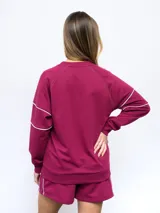 Buzo a la base de felpa color gris claro, sin friza, con cuello redondo y logo Umbro bordado en el pecho. Presenta pipings en contraste color borgoña en hombros y puños.