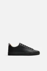 Zapatilla urbana de cuero sintético color negro, con cordones y suela plana.