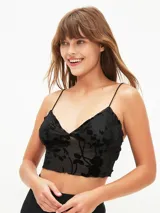 Top corto negro de tirantes finos, con escote en V y borde festoneado. El tejido es transparente con un estampado de terciopelo floral en relieve.