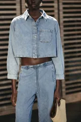 Camisa corta de denim celeste, con cuello solapa, manga larga, bolsillo delantero de plastrón y cierre frontal con botones metálicos.