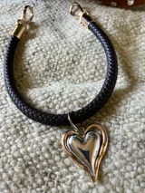 Gargantilla marrón con dije plateado en forma de corazón con borde dorado.