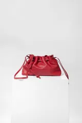 Bolso tipo sobre de cuero color rojo, con frunce superior y cierre con cordones. Tiene correa larga desmontable y bolsillo interno con cierre.