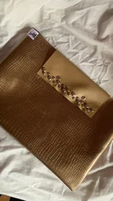 Funda para laptop color dorado con textura símil piel de cocodrilo y solapa color beige con apliques de tachas plateadas.
