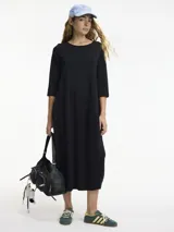 Vestido negro de manga 3/4 con cuello redondo y bolsillos laterales. Combina texturas de algodón y lino.
