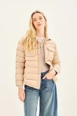 Campera puffer color beige con cuello camisero, cierre con botones a presión, bolsillos con solapa en el pecho y relleno de plumas.