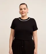 Blusa negra de algodón con cuello redondo y mangas cortas. Presenta aplicación de perlas artificiales y strass en el cuello.