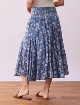 Falda midi de algodón estampada con flores blancas sobre fondo azul. Tiene pretina ancha elastizada en punto smock, ruedo con volados y forro interno a tono.