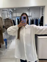 Camisa blanca con pequeños brillos, de corte oversize, con cuello clásico y mangas largas abotonadas.