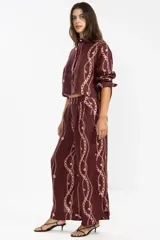 Pantalón de lino italiano color borgoña con estampado de cadenas en color rosa. De corte recto y talle medio, con cintura elástica en la parte posterior, bolsillos delanteros y aberturas laterales en el ruedo.